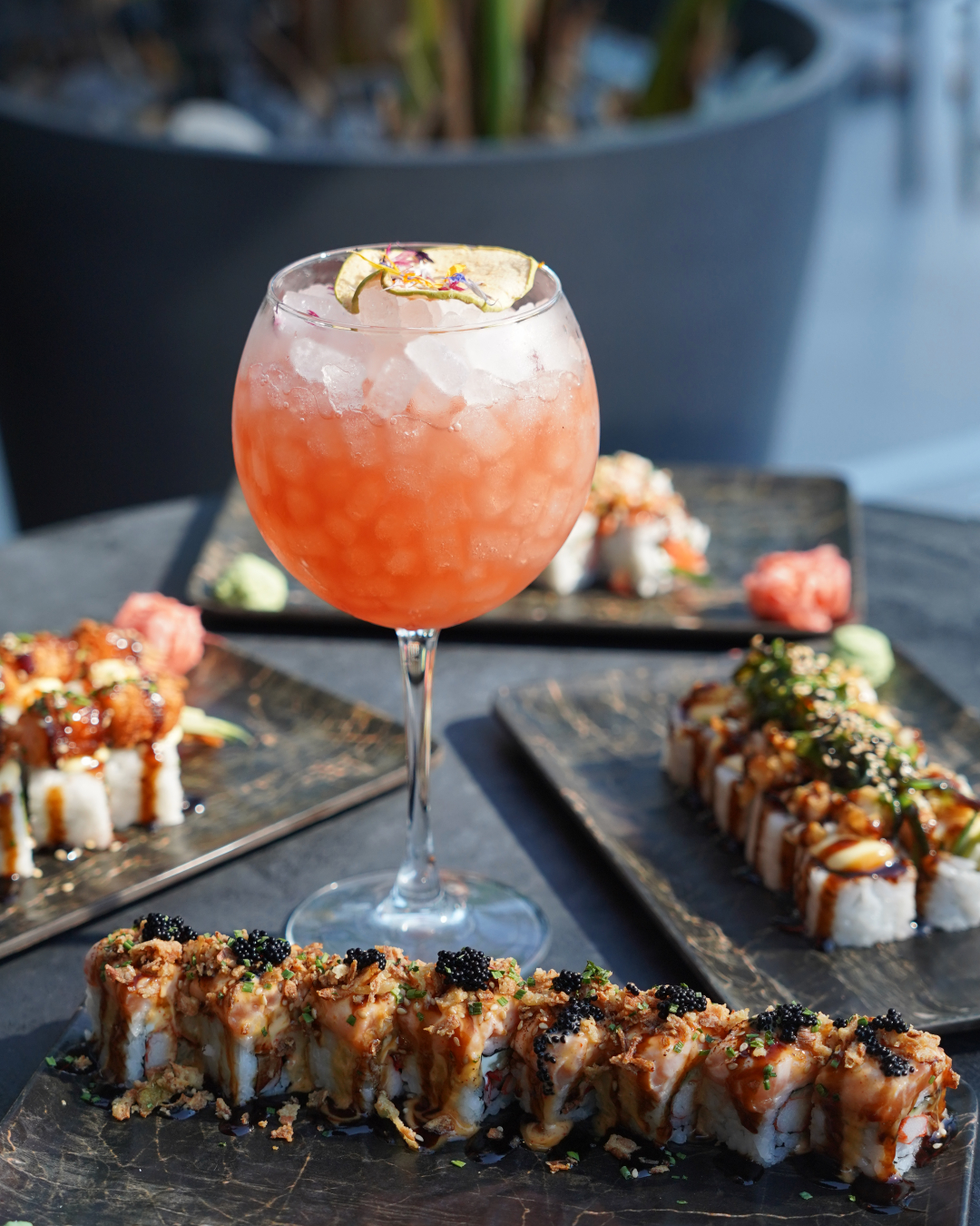 Signature pink cocktail on crushed ice beside sushi at Barok