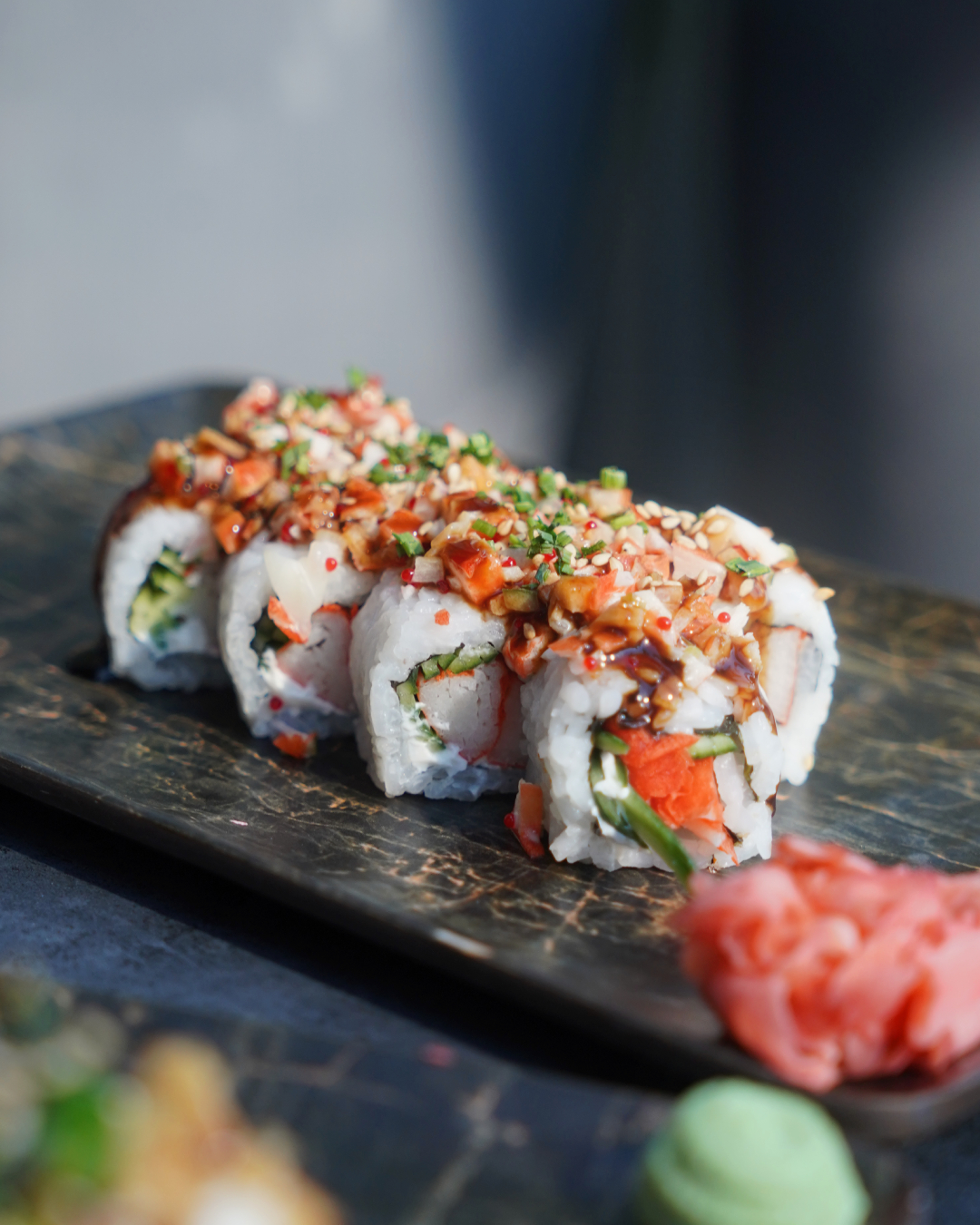 Close-up of a topped sushi roll with sesame and chilli on slate